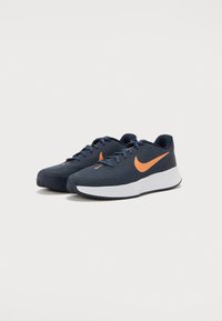 Blå idrettssko med et strukturert mesh-overdel, oransje Nike Swoosh og hvit mellomsåle. Har en snørelukking og mønstret yttersåle.