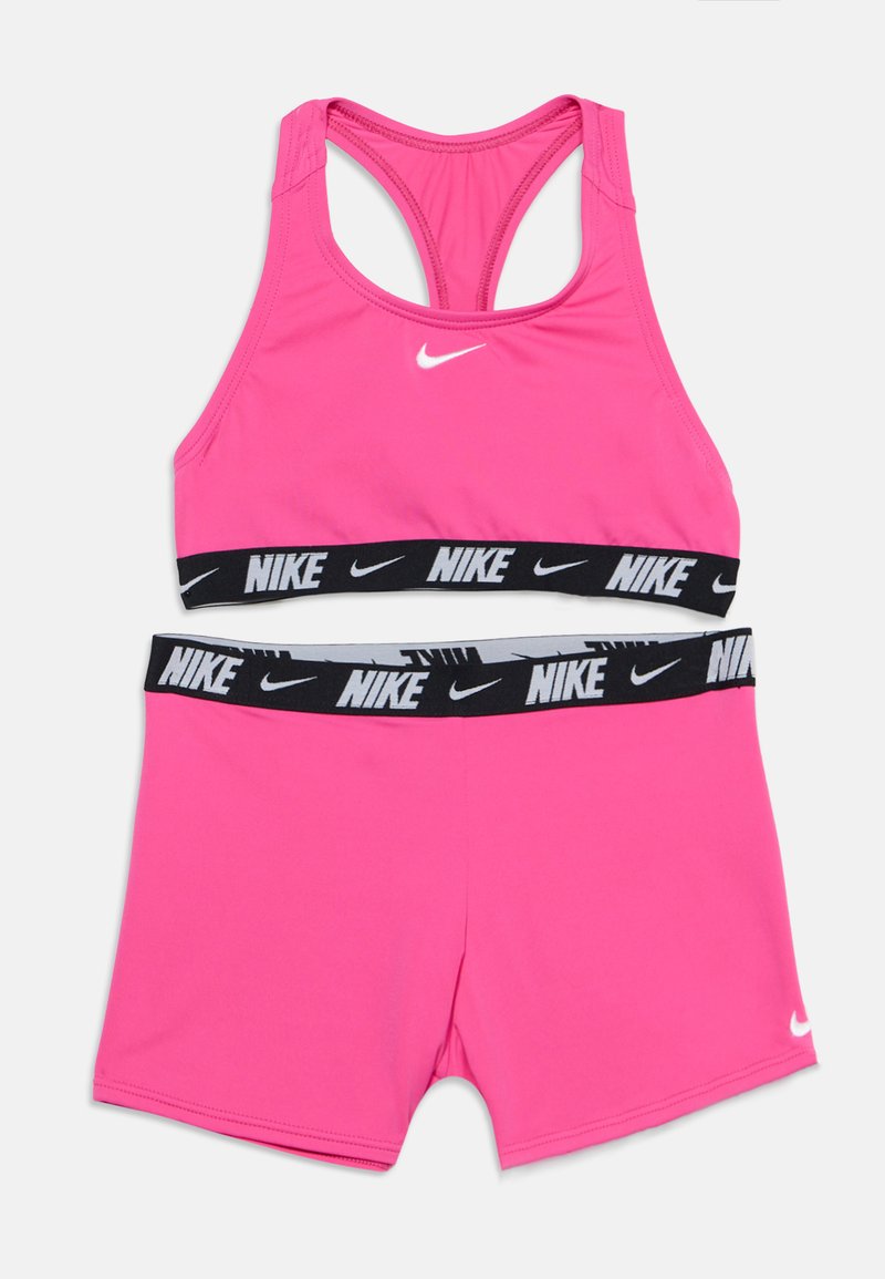 Φωτεινό ροζ σετ αθλητικού σουτιέν και σορτς Nike με μαύρες ελαστικές ταινίες που έχουν λευκά λογότυπα και σχήματα Nike.