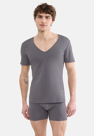 Young man wearing matching gray V-neck short-sleeve shirt and boxer briefs, standing against a plain light background.