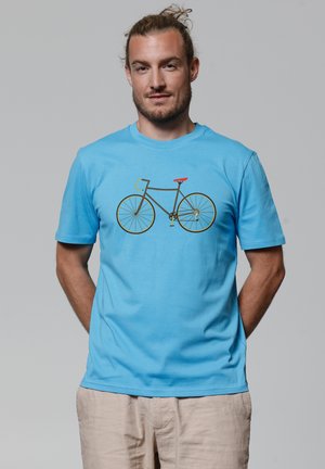 Lichtblauwe katoenen T-shirt met een grafisch ontwerp van een fiets in zwart en goud, met een rode accentkleur op het stuur. Korte mouwen, ronde hals.