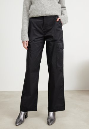 Black cargo pants with a loose fit, made of smooth material, featuring large side pockets and contrasting stitching. Paired with silver heeled boots.