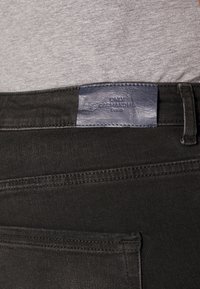 Zwarte spijkerbroek met een gladde textuur, voorzien van een leren merklabel in marineblauw met de naam "ONLY CARMAKOMA". Voorzien van standaard zakdetails.