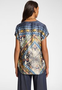 Blusa a maniche corte con un motivo geometrico colorato nei toni del blu, arancione e giallo, realizzata in un tessuto morbido e fluido, con orlo arrotondato.