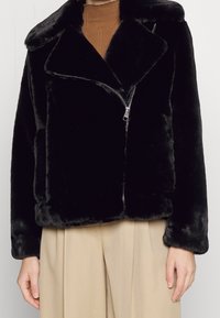 Sort jakke i falsk pels med notched krave, lukkes foran med lynlås og sidelommer. Blød tekstur, kort design og oversized pasform.