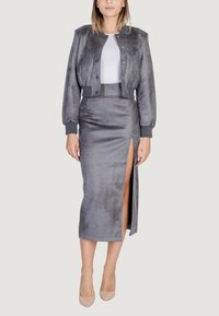 Chaqueta bomber gris hecha de tela suave con puños acanalados, combinada con una falda lápiz gris con una abertura en el muslo, complementada con tacones nude.
