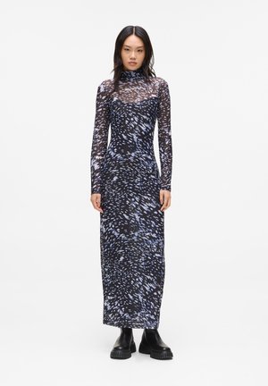 Robe ajustée à manches longues en noir avec un motif abstrait bleu, dotée d'un col montant et d'une texture en dentelle transparente. Portée avec des bottes noires.