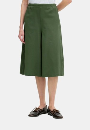 Persona che indossa pantaloni verde oliva a gamba larga lunghezza al ginocchio con vita elastica e mocassini marrone scuro con lacci.