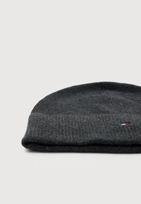 Beanie a coste di un grigio scuro con un piccolo logo rettangolare rosso, bianco e blu vicino al bordo piegato, su uno sfondo bianco.