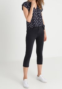 Marinblus med blommönster och korta ärmar, kombinerad med figurnära svarta caprijeans och vita sneakers. Slät tygkvalitet, avslappnad passform.