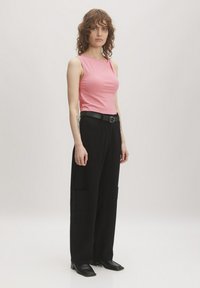 Roze mouwloze top, zwarte wijde broek met zakken, gestructureerde stof, zwarte riem en puntige zwarte schoenen. Eenvoudig en modern ontwerp.