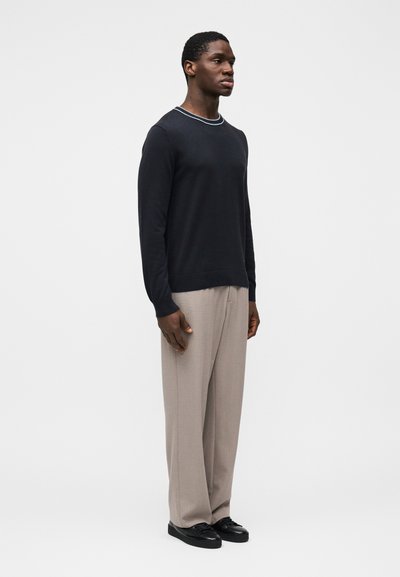 Pull bleu marine à col rond avec un détail de rayure claire au niveau du col, associé à un pantalon beige clair et des baskets noires.