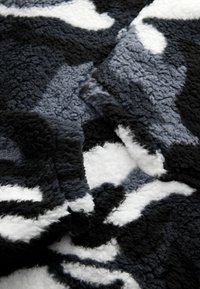 Zwarte, grijze en witte fleece deken met een gestructureerd, comfortabel oppervlak. Heeft een camouflagepatroon van zacht, pluizig materiaal.