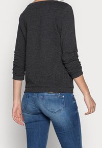 Tmavě šedý svetr s texturou, dlouhými rukávy a žebrovanými manžetami, kombinovaný s úzkými modrými džínami s jemným designem kapes.