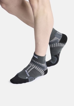 Grijze en zwarte gevoerde sokken tot aan de enkel, gedragen op bleke benen, met geometrische patronen en merkmarkeringen.