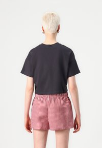 Black cropped t-shirt with short sleeves paired with red and white gingham patterned shorts featuring an elastic waistband.
