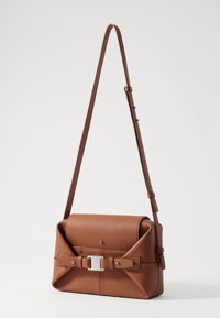 Brown leather crossbody bag with a structured design, featuring a rolled flap, silver hardware, and a buckle accent on the front.