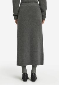 Lång, grå stickad kjol med ribbad textur, hög midja och rak skärning, matchad med grå strumpor och svarta klackskor.