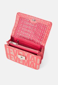 Koralfarvet Steve Madden pung med geometrisk logo mønster, åben for at vise indvendige lynlås- og slip-lommer samt sølvfarvet lås.