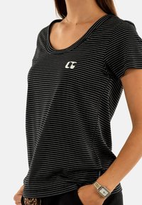 Camiseta de manga corta a rayas en blanco y negro con escote redondeado y un pequeño logo en el pecho, hecha de una tela suave y ligera.