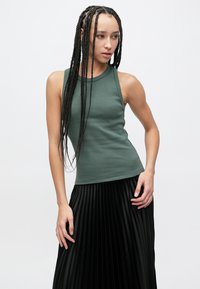 Top verde scuro senza maniche a coste abbinato a una gonna nera plissettata. Il top ha una forma aderente e una scollatura rotonda.