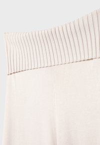 Giro in vita di un beige chiaro con righe verticali, abbinato a un tessuto liscio, che crea una vestibilità rilassata, progettato per il comfort e la versatilità.