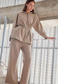 Beżowy hoodie z długimi rękawami, regulowany w pasie, z zamkiem błyskawicznym, w zestawie z szerokimi beżowymi spodniami. Miękki materiał o gładkiej strukturze. Minimalistyczny design.