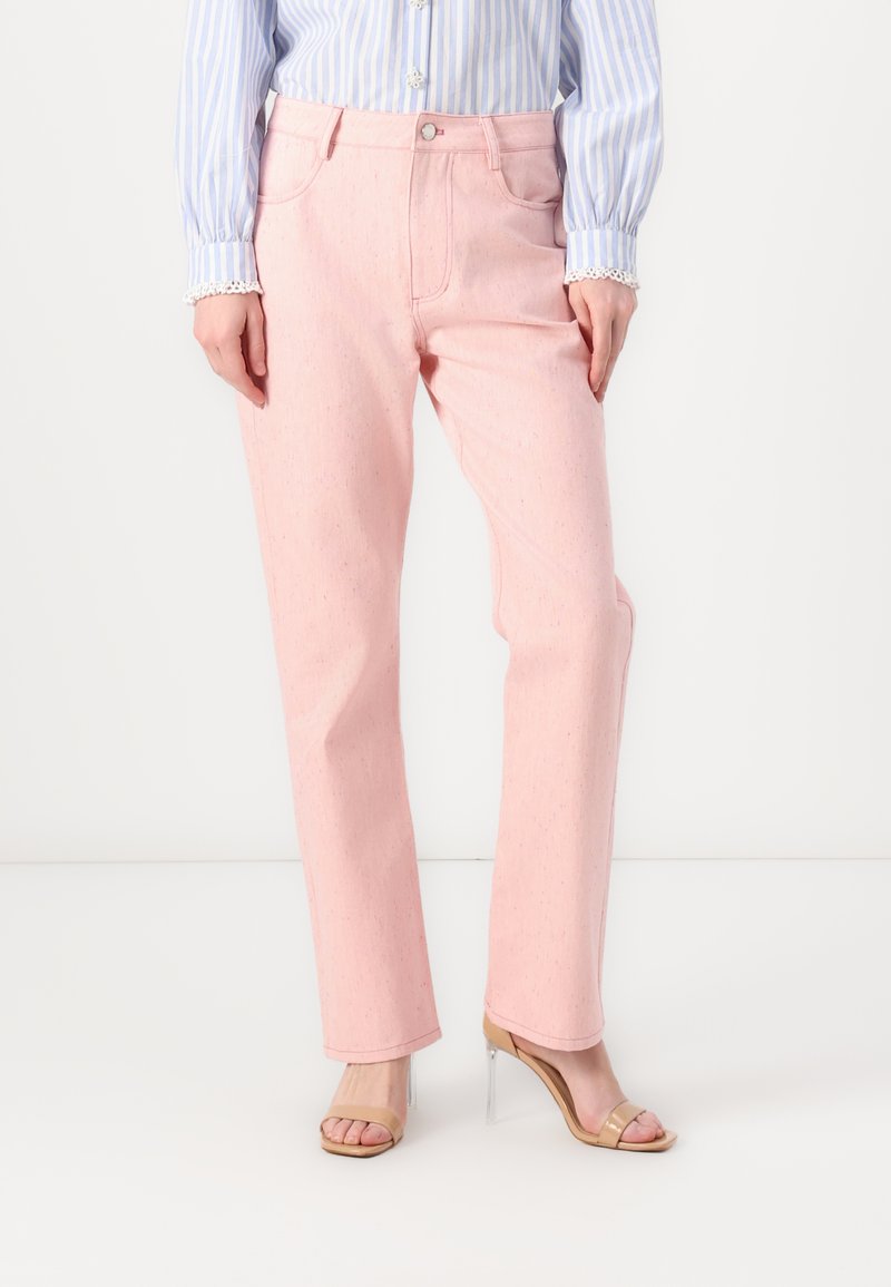 Pantalones de mezclilla rosa claro con pierna recta, diseño de cinco bolsillos y botón plateado mate. Combinados con una camisa azul a rayas y tacones transparentes.