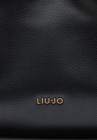 Melna teksturēta ādas soma ar zelta "LIU·JO" logo apakšā, ar gludu, elegantu apdari un minimālistisku dizainu.