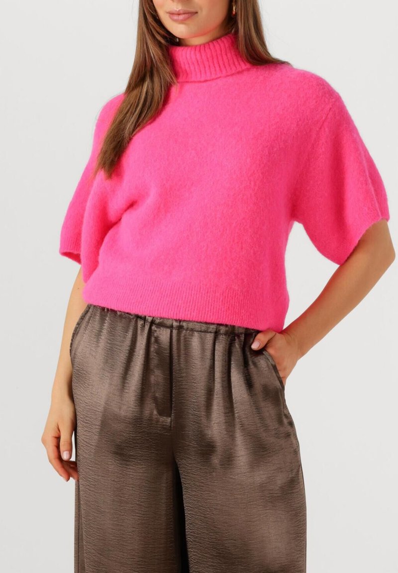 Fuchsia gebreide trui met korte mouwen en een hoge geribbelde kraag, gecombineerd met brede bruine satijnen broek. Soepele textuur en relaxte pasvorm.