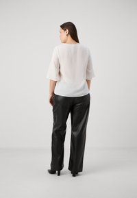 Lett, kremfarget bluse med firkantet utringning og flytende bell-ermer, kombinert med blanke svarte skinnbukser. Glatt tekstur, minimalistisk design.