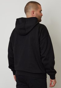 Černá mikina s kapucí z měkké látky. Má uvolněný střih, ribované manžety a klokaní kapsu. Je jednoduchá, bez viditelných log.