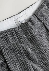 Graues Herringbone-Mustergewebe mit Falten, ausgestattet mit einem weißen Innenfutter und einem Etikett mit der Aufschrift "N. PREMIUM COLLECTION."