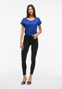 Top azul de manga corta con escote redondo, combinado con vaqueros negros ajustados y tacones abiertos negros. Tela suave y diseño ajustado.