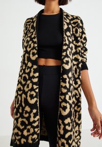 Leopardmönstrad kofta i svart och beige, öppen front, lång ärm, ribbad mudd, mjuk textur, matchad med en svart crop top och byxor.