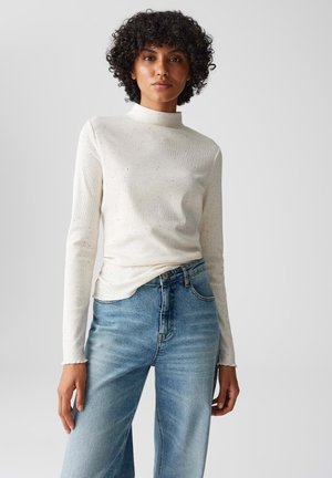 Lichtbeige lange mouw top met een hoge halslijn en gestructureerde textuur, gecombineerd met lichtblauwe high-waisted denim jeans.