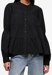 Blusa nera in cotone con una chiusura a bottoni frontale, volant arricciati e maniche a palloncino voluminose. Texture liscia con una silhouette strutturata.