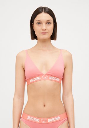 Rozā kokvilnas bralette ar plānām siksniņām un dziļu V-veida kakla izgriezumu. Iezīmēta ar balto logotipa joslu ar lāča dizainu. Gluda tekstūra, minimālisma stils.