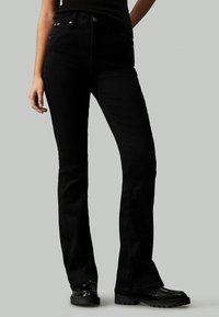 Pantalones vaqueros de campana negros con un diseño elegante, fabricados en tejido de denim, que cuentan con cinco bolsillos y cierre de botón. Ajuste en la cintura natural con una textura suave.