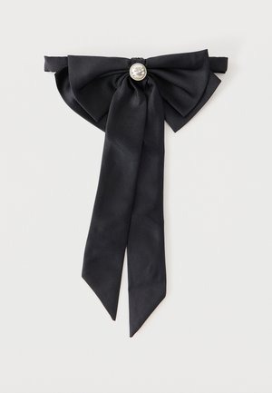 Schwarze Stofffliege mit langen Enden und einem zentralen silbernen Zierknopf auf grauem Hintergrund.