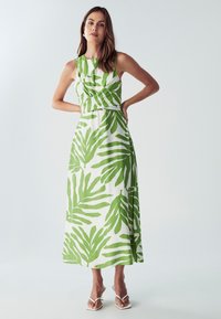 Maksi haljina s uzorkom zelenog lišća na bijeloj tkanini. Haljina bez rukava s prilagođenim korzetom i lepršavom suknjom. Lagani i teksturirani materijal.