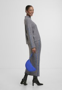 Grau gerippter Strickanzug mit blauen Seitenstreifen, bestehend aus einem Pullover mit hohem Kragen und einem langen Rock. Blaue Halbmoney-Handtasche und hohe schwarze Stiefel.