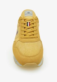 Zapatilla deportiva amarilla hecha de tela texturizada con acentos de ante, que presenta cordones planos, un logo y una franja triangular en rojo, blanco y azul.