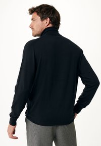 Svart träningströja med hög krage, långa ärmar och ribbade ärmslut, visad bakifrån mot en vit bakgrund.