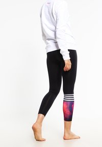 Černé legíny s multicolor galaktickým vzorem na dolní části nohy a třemi bílými horizontálními pruhy na lýtku. Materiál z bavlněné směsi.