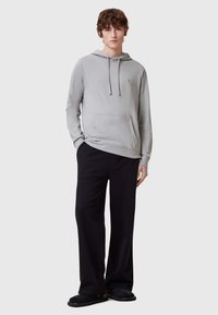 Sudadera de color gris claro hecha de un tejido suave, con un bolsillo frontal, capucha con cordones y pantalones negros de corte holgado con una textura suave.