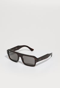 Ochelari de soare din scoică cu ramă pătrată, lentile gri și logo auriu pe braț. Textură netedă și design robust.