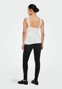 Hvid tanktop med blonde stropper, parret med sorte skinny jeans og sorte loafers. Toppen har en glat tekstur og tætsiddende design.