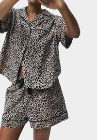Piżama w wzór panterki z krótkim rękawem, wykonana z miękkiego materiału, z koszulą zapinaną na guziki oraz dopasowanymi szortami z czarnymi lamówkami i regulowanym pasem.