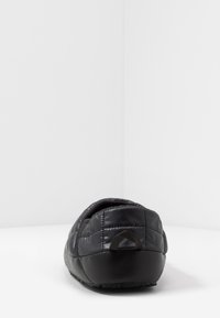 Black slipper with quilted texture and plush lining, featuring a sturdy rubber sole and a pull tab at the back for easy wear.