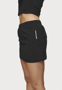 Sorte cargo shorts i svart med teksturert stoff, elastisk midje og en sidelomme med merkevarenavnet "PEGADOR" i hvit skrift.